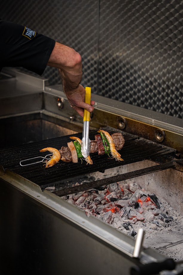 Chef grilling skewers over charcoal